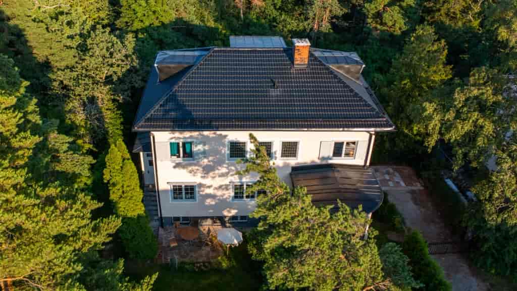 Vit villa med svart tak bland tallar, drönarbild