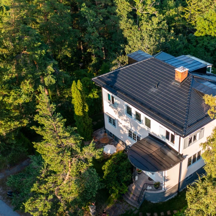Vit villa med svart tak bland träd, sedd ovanifrån