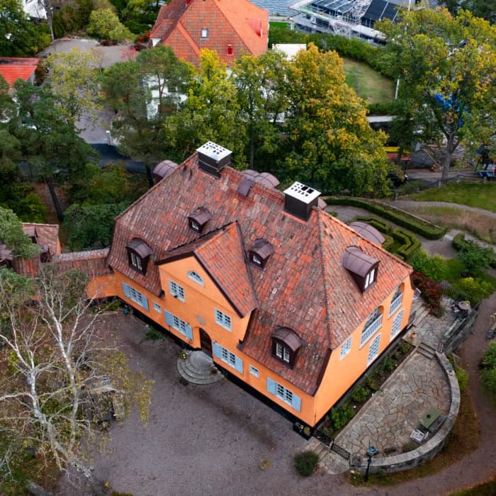 Gul villa med rött tegeltak och takkupor, drönarbild