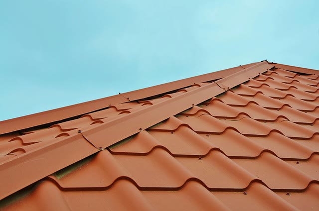 Rött plåttegel längs taknocken mot blå himmel