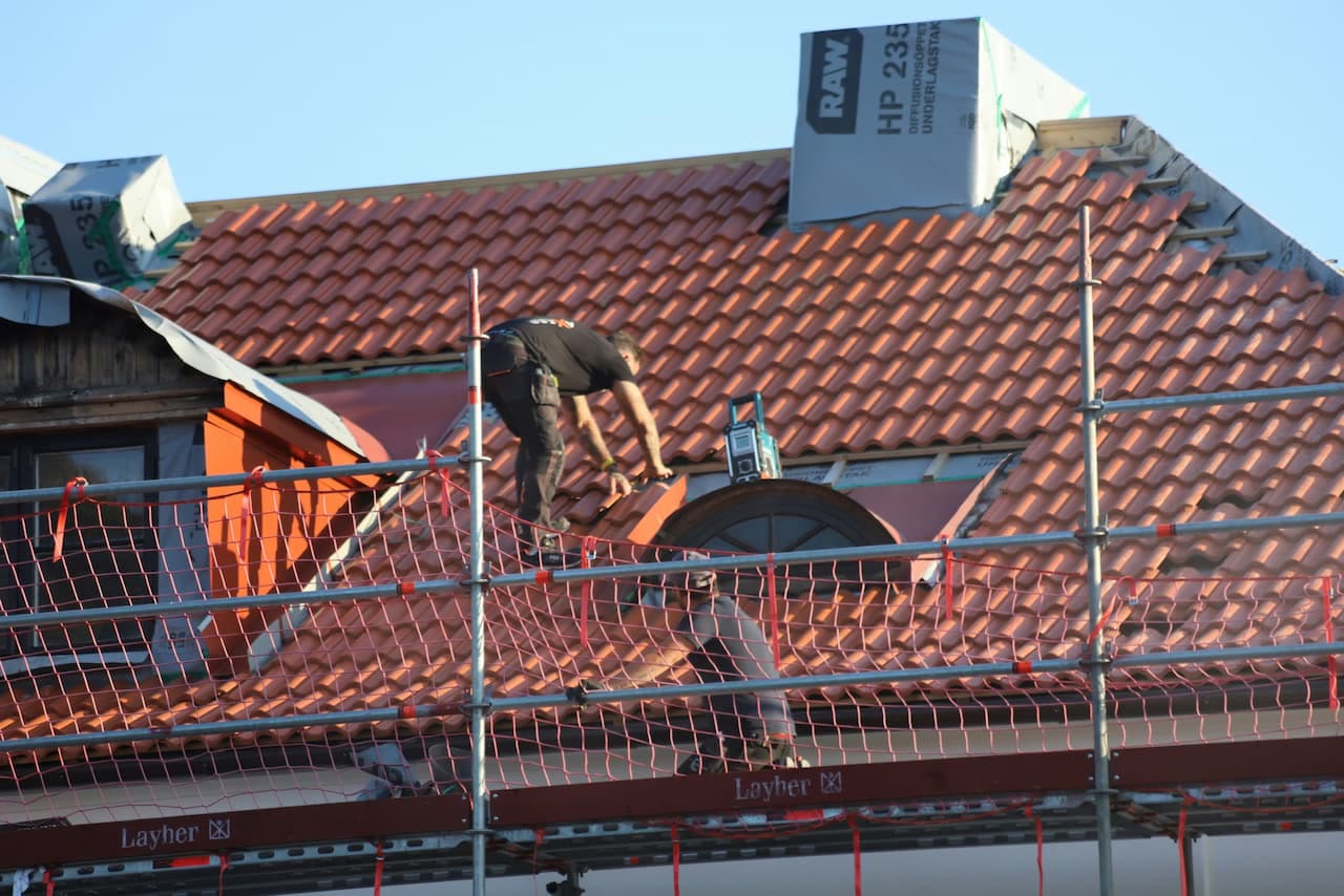Takläggare lägger röda takpannor bakom ställning med skyddsnät